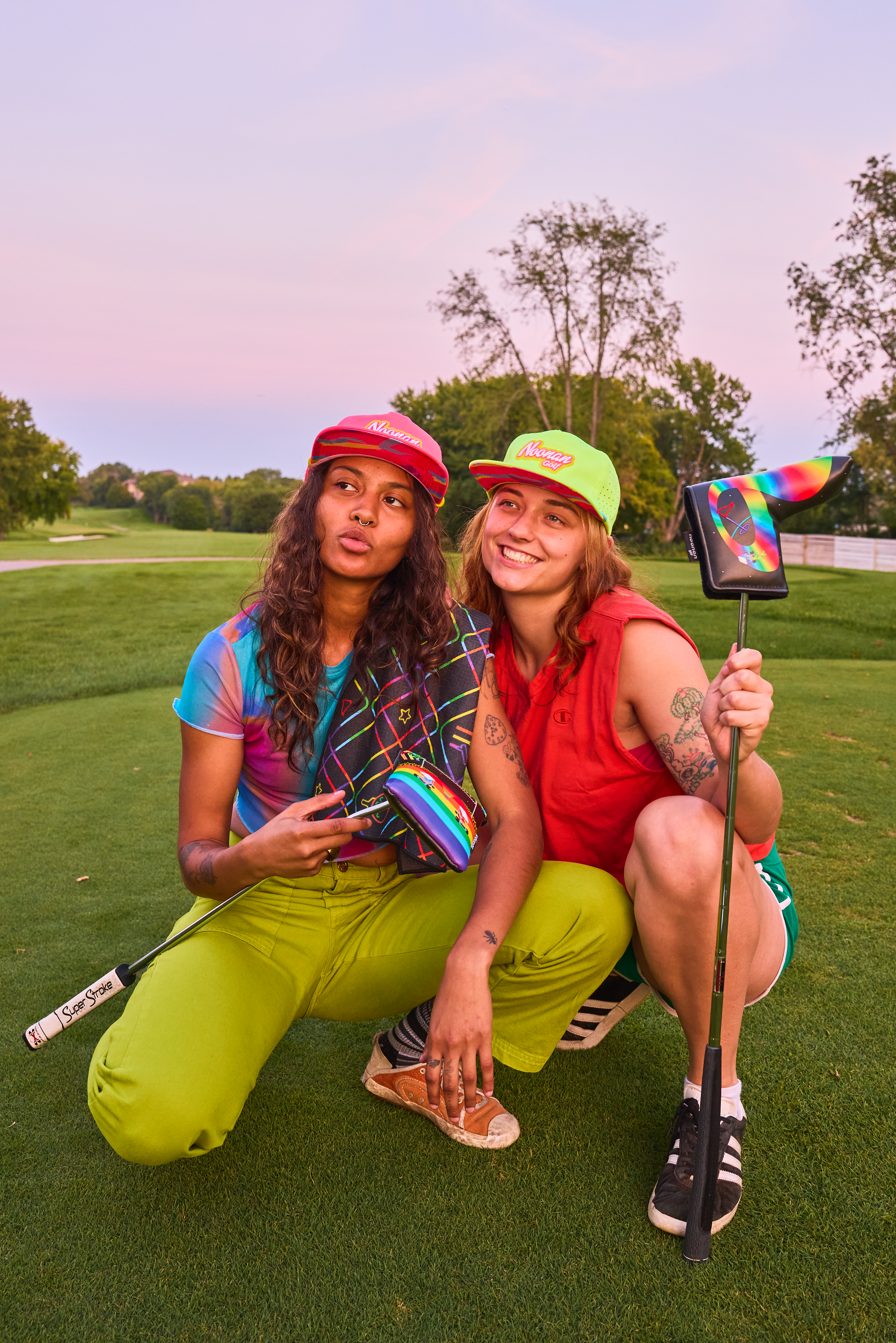 Two women on a golf course holding noonan golf putter covers and accessories